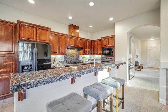 kitchen featuring kitchen peninsula, a breakfast bar area, backsplash, light colored carpet, and black appliances