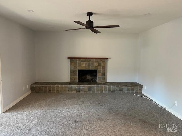 unfurnished living room featuring ceiling fan, carpet floors, and a tiled fireplace