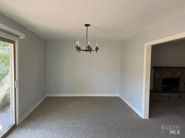 carpeted empty room featuring baseboards, a tile fireplace, and a notable chandelier