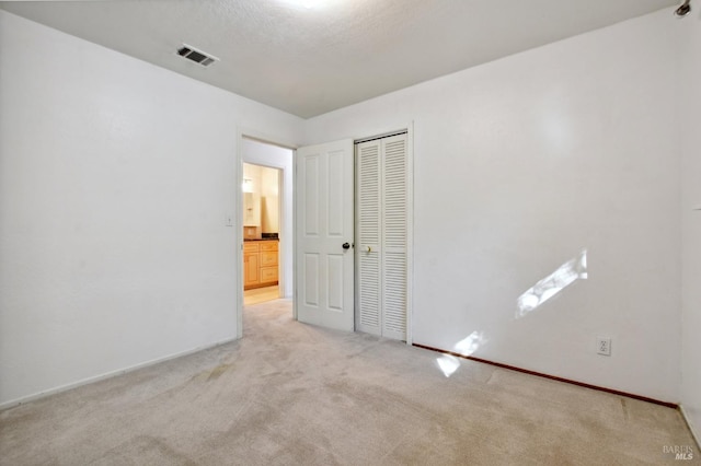 unfurnished bedroom featuring a textured ceiling, light carpet, and a closet