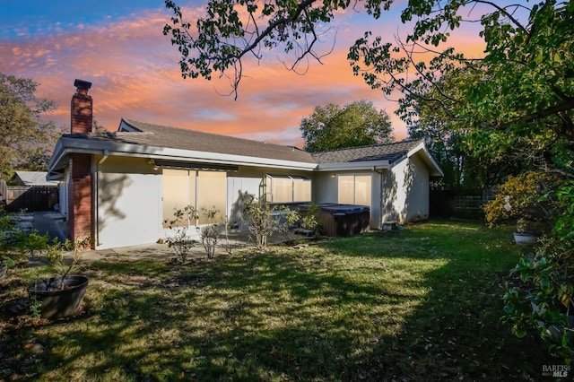 back house at dusk with a patio area, a yard, and a hot tub