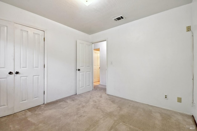 unfurnished bedroom with light carpet, a closet, and a textured ceiling