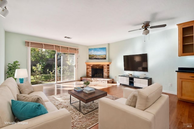 living room with ceiling fan, light hardwood / wood-style floors, and a brick fireplace