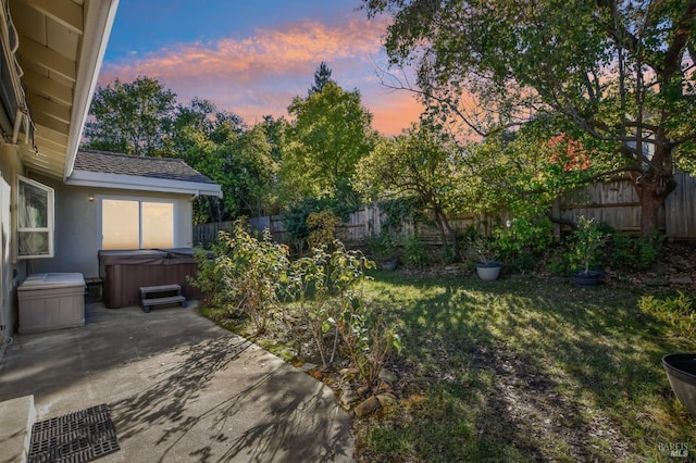 yard at dusk with a hot tub and a patio area