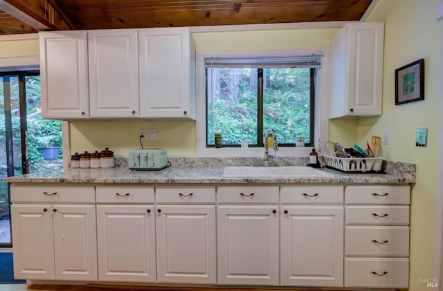 kitchen featuring light stone counters, a sink, a wealth of natural light, and white cabinets