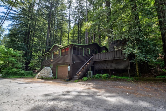 view of front of property with a view of trees, an attached garage, stairs, a deck, and ac unit