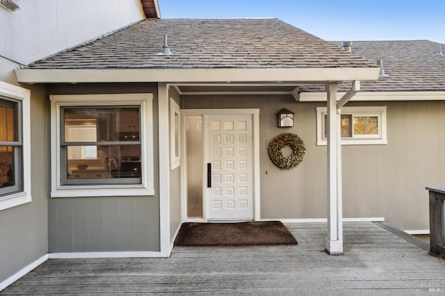 view of exterior entry featuring a shingled roof and a deck