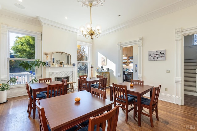 dining area featuring crown molding, a tiled fireplace, dark wood-type flooring, and an inviting chandelier