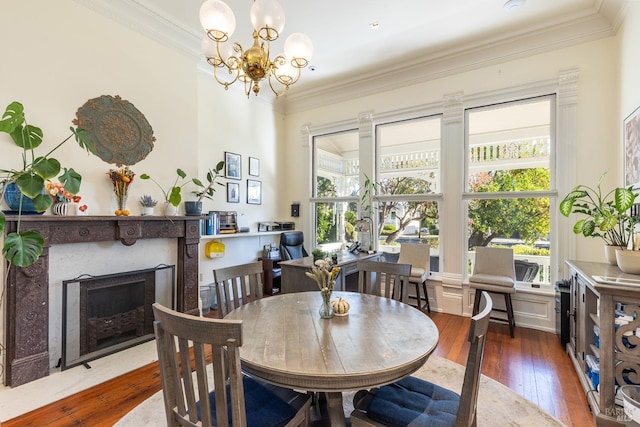 dining room featuring a fireplace, wood-type flooring, an inviting chandelier, and ornamental molding