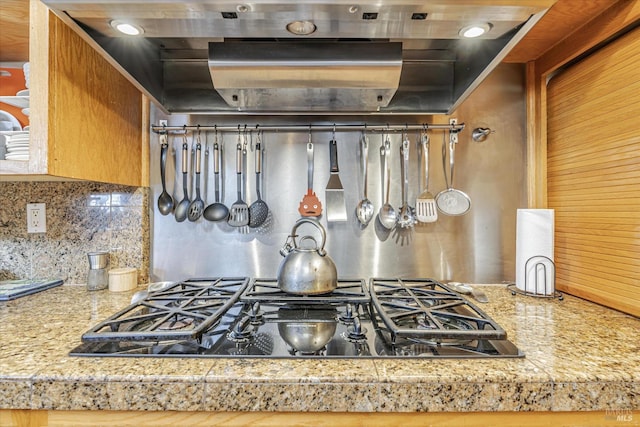 kitchen with black gas cooktop, wall chimney range hood, and backsplash