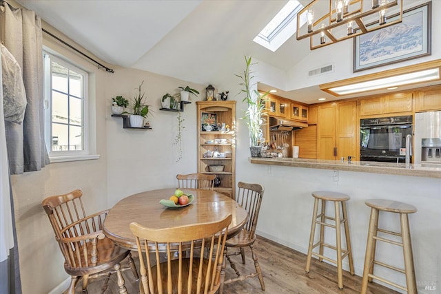 dining room featuring light wood-type flooring, vaulted ceiling with skylight, and visible vents