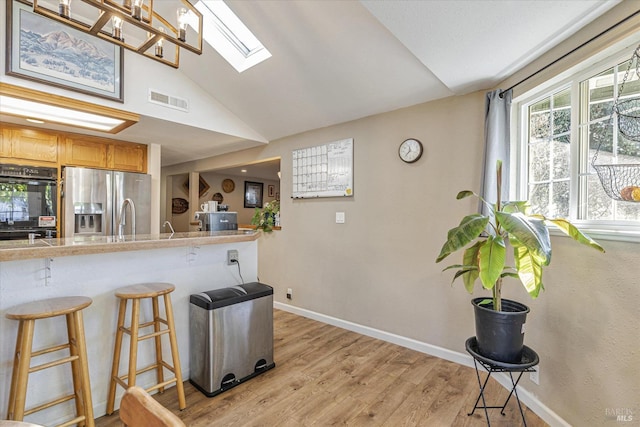 kitchen featuring a breakfast bar, stainless steel fridge with ice dispenser, visible vents, light wood-type flooring, and baseboards