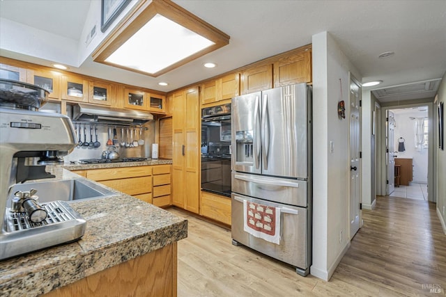 kitchen featuring dobule oven black, light wood-style floors, stainless steel fridge with ice dispenser, under cabinet range hood, and gas stovetop