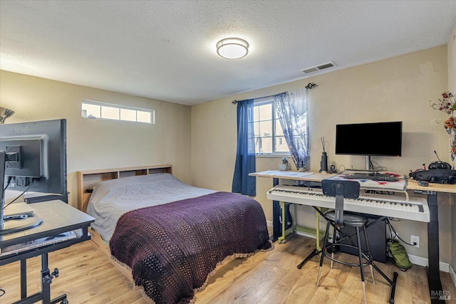 bedroom with visible vents, a textured ceiling, multiple windows, and wood finished floors