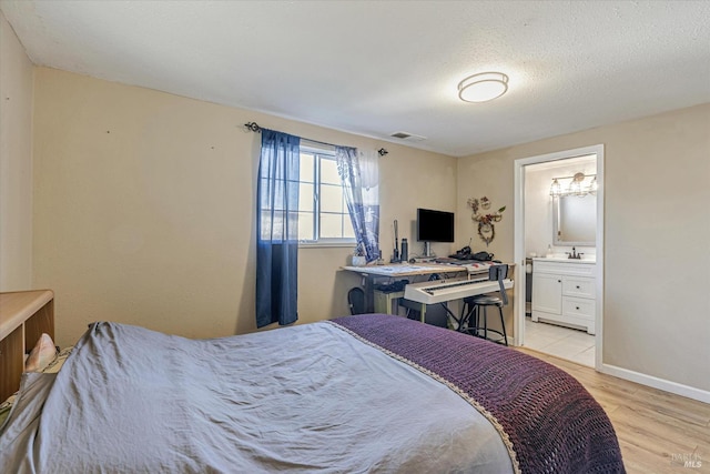 bedroom with a sink, visible vents, baseboards, light wood-style floors, and ensuite bath