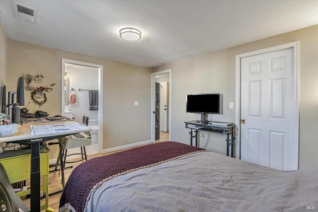 bedroom with visible vents, ensuite bath, a textured ceiling, and baseboards