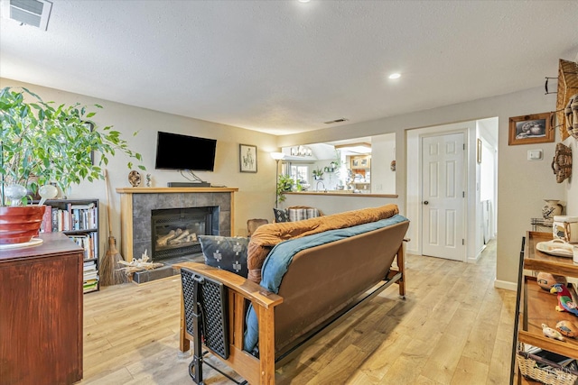 living area with light wood-style floors, a tile fireplace, visible vents, and a textured ceiling