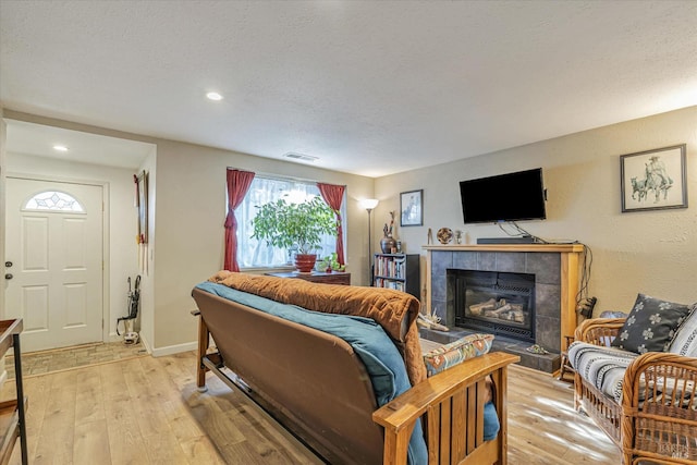 living room featuring light wood finished floors, a textured ceiling, visible vents, and a tiled fireplace