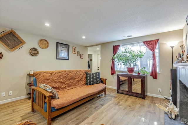 living room featuring baseboards, visible vents, light wood-style flooring, a textured ceiling, and a fireplace