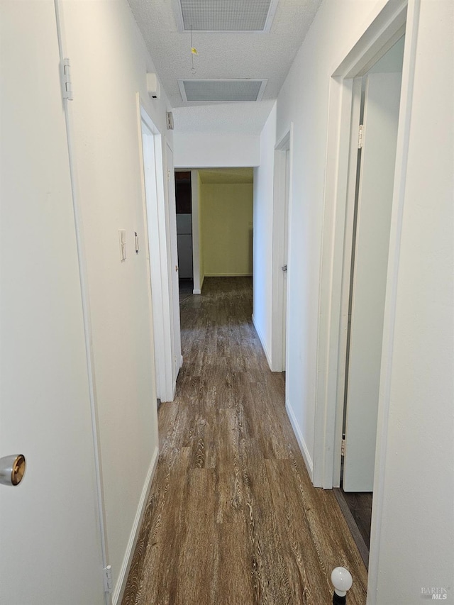 corridor with a textured ceiling and dark hardwood / wood-style flooring