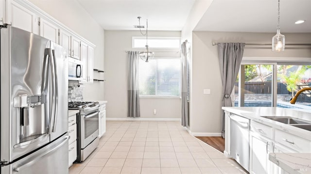 kitchen with light tile patterned flooring, white cabinets, stainless steel appliances, and decorative light fixtures