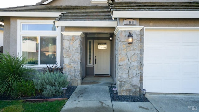 doorway to property featuring stone siding, an attached garage, and stucco siding