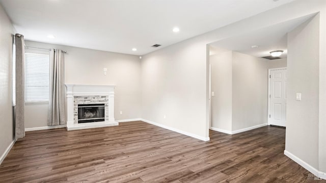 unfurnished living room with dark hardwood / wood-style floors and a stone fireplace