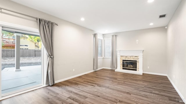 unfurnished living room featuring wood finished floors, a brick fireplace, baseboards, visible vents, and recessed lighting