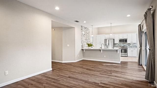 kitchen with dark wood-type flooring, white cabinets, a kitchen breakfast bar, appliances with stainless steel finishes, and decorative light fixtures