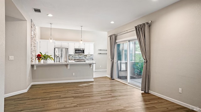 kitchen with hanging light fixtures, stainless steel appliances, kitchen peninsula, a kitchen bar, and white cabinets