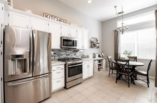 kitchen featuring pendant lighting, white cabinets, decorative backsplash, light tile patterned floors, and appliances with stainless steel finishes