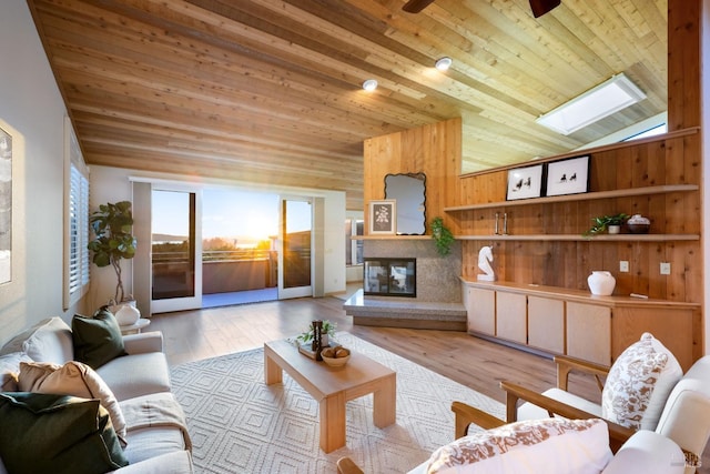 living room featuring a premium fireplace, light hardwood / wood-style flooring, lofted ceiling with skylight, wooden walls, and wood ceiling