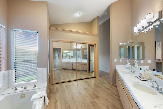 bathroom featuring hardwood / wood-style flooring, vanity, a tub to relax in, and high vaulted ceiling