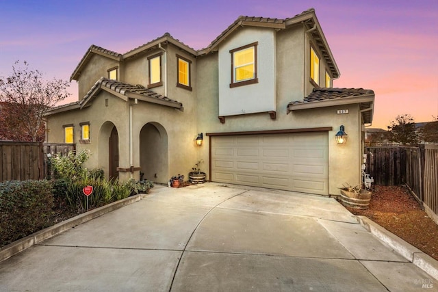 mediterranean / spanish-style home with fence, stucco siding, a tiled roof, an attached garage, and driveway