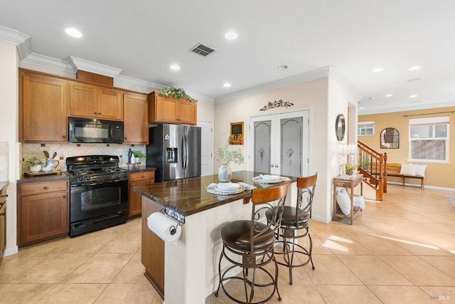 kitchen featuring a kitchen island, a breakfast bar, tasteful backsplash, light tile patterned floors, and black appliances