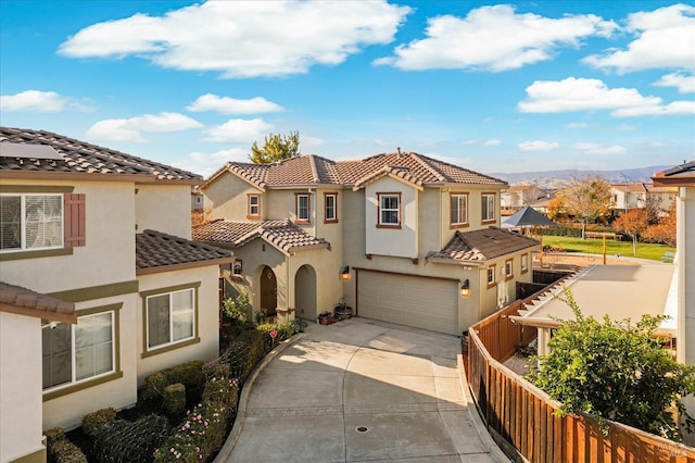 mediterranean / spanish home featuring driveway, a tile roof, a residential view, fence, and an attached garage