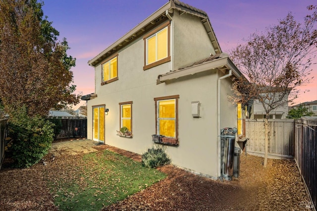 back of property at dusk featuring a fenced backyard and stucco siding