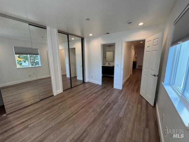 unfurnished bedroom featuring multiple closets, connected bathroom, and dark hardwood / wood-style floors