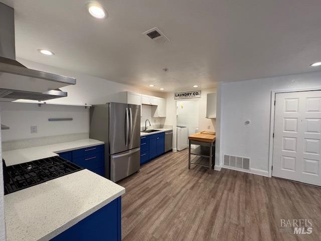 kitchen with appliances with stainless steel finishes, white cabinetry, blue cabinetry, sink, and dark hardwood / wood-style floors