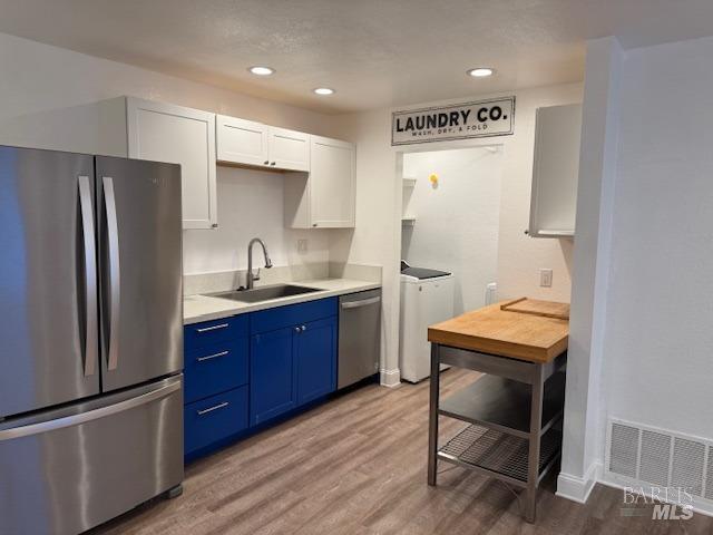 kitchen featuring sink, appliances with stainless steel finishes, independent washer and dryer, and white cabinetry