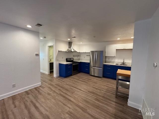 kitchen featuring sink, appliances with stainless steel finishes, blue cabinets, white cabinets, and wall chimney exhaust hood