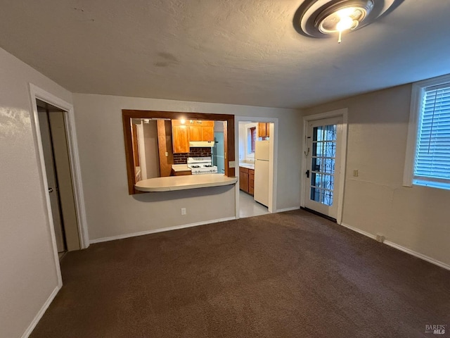 unfurnished living room with a textured ceiling, carpet floors, and baseboards