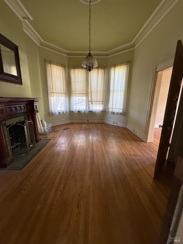 unfurnished living room with ornamental molding, a fireplace with raised hearth, baseboards, and wood finished floors