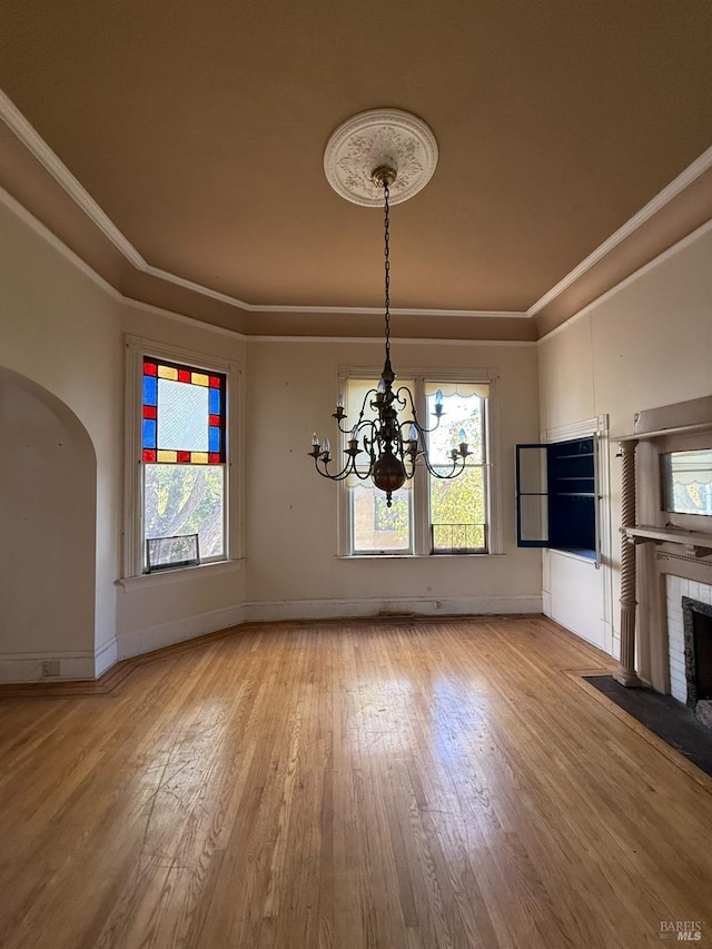 unfurnished dining area with arched walkways, a notable chandelier, light wood-style floors, a brick fireplace, and crown molding