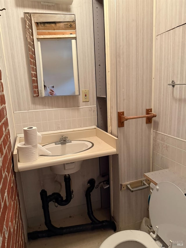 bathroom with toilet, a sink, and tile walls