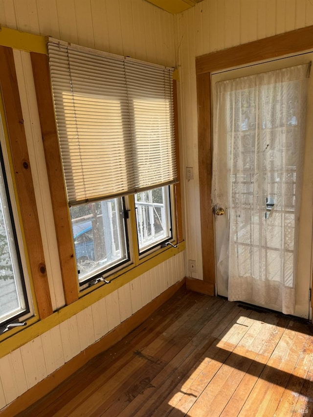 unfurnished room with wood walls, hardwood / wood-style flooring, and baseboards