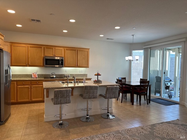 kitchen featuring sink, light tile patterned floors, an island with sink, decorative light fixtures, and stainless steel appliances