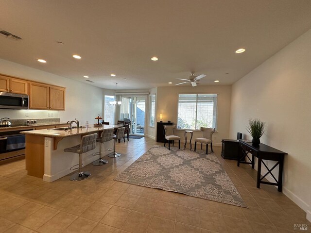 kitchen with ceiling fan, sink, a kitchen bar, a kitchen island with sink, and appliances with stainless steel finishes