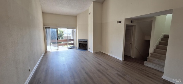 unfurnished living room with hardwood / wood-style flooring, a textured ceiling, and a towering ceiling