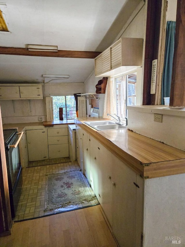 kitchen with black electric range, beam ceiling, light countertops, light wood-style floors, and a sink